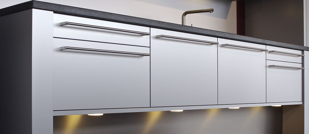This creative quality kitchen has a sink bridge construction with ground clearance. The made-to-measure stainless steel bar handles for the aluminium fronts can only be provided by a real kitchen specialist.